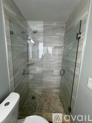 A bathroom with a glass shower stall and a toilet.