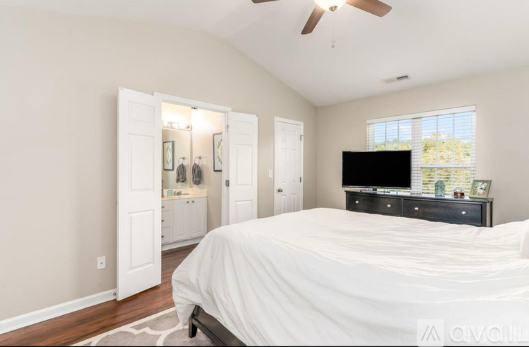A bedroom with a large bed, a dresser with a TV on top, and a ceiling fan.