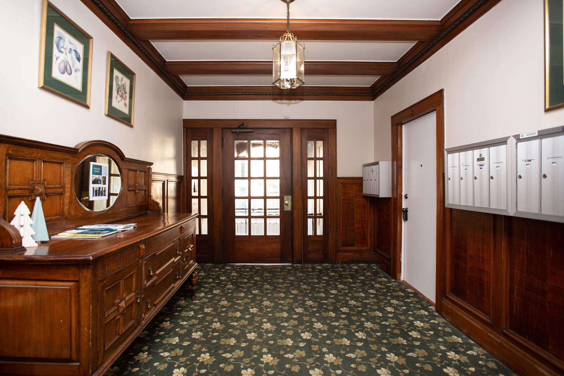 A hallway with a wooden floor and ceiling, a chandelier, and a row of lockers on the right.