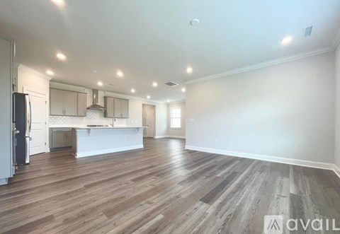 A spacious room with wooden flooring and a kitchen area with white appliances.