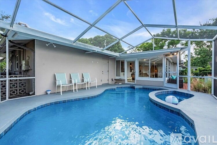 A swimming pool in a sunroom with white chairs.