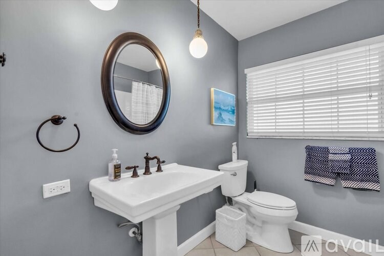 A bathroom with a white sink and toilet, a round mirror, and a light bulb hanging from the ceiling.