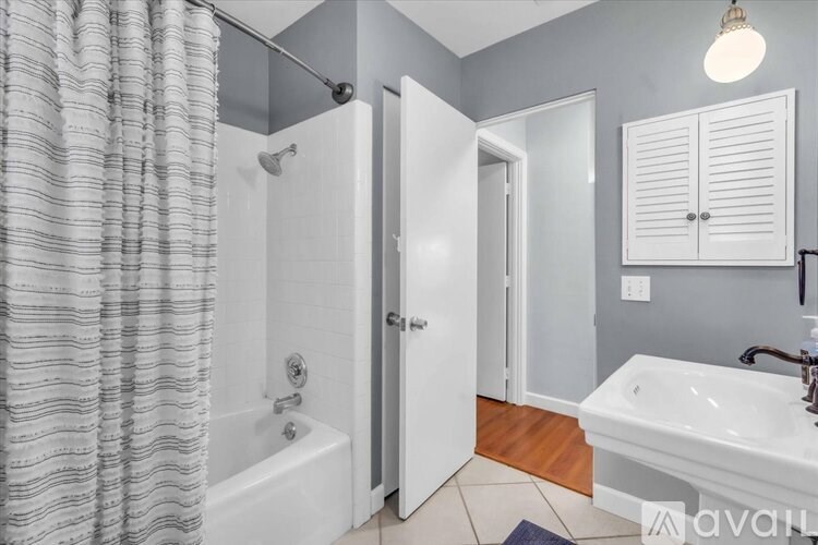 A bathroom with a white tub and sink, a shower curtain, and a wooden floor.