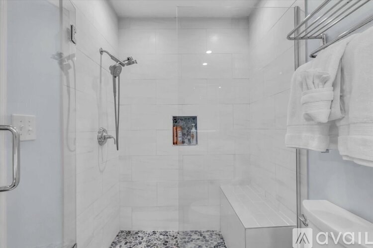 A white tiled bathroom with a walk-in shower and a towel rack.