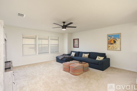 A living room with a blue couch, a ceiling fan, and a painting on the wall.