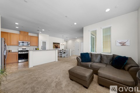 A living room with a brown leather couch and a kitchen area in the background.