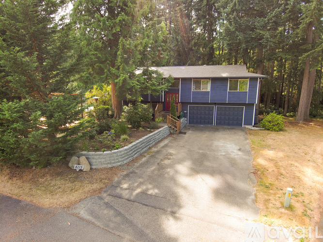 A blue house with a garage is surrounded by trees.