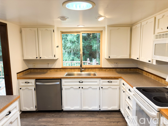 A kitchen with white cabinets and a window overlooking a green area.