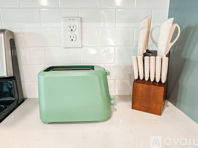 A green toaster and a wooden holder with white towels are on a countertop.