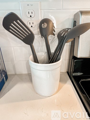 Utensils in a white cup on a kitchen counter.
