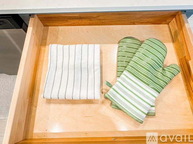 A pair of green striped oven mitts and a white striped towel in a wooden drawer.