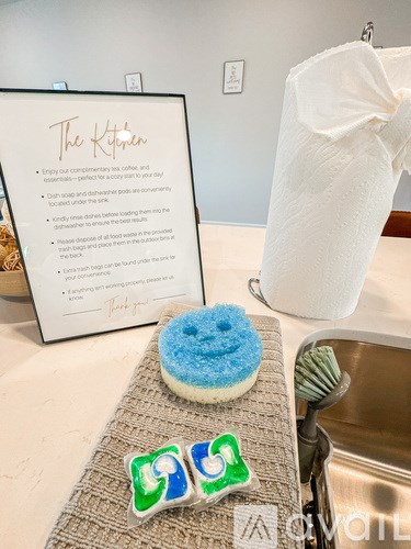 A sign titled "The Kitchen" with a list of instructions next to a sink and a donut with a smiley face on a mat.
