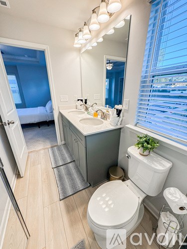A bathroom with a toilet, sink, mirror, and a window with blinds.