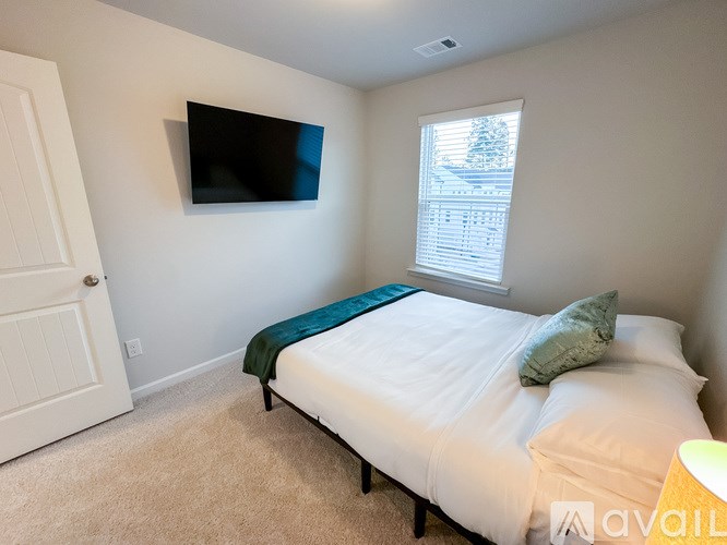 A bedroom with a bed, a window, and a flat screen TV mounted on the wall.