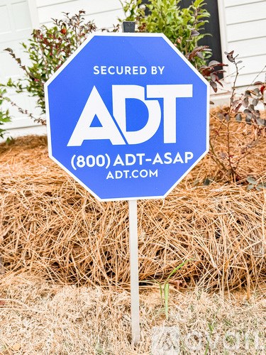 A blue sign that says "SECURED BY ADT" is in front of a white house.