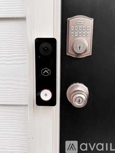 A black door with a silver lock and a black device with a red light on it.