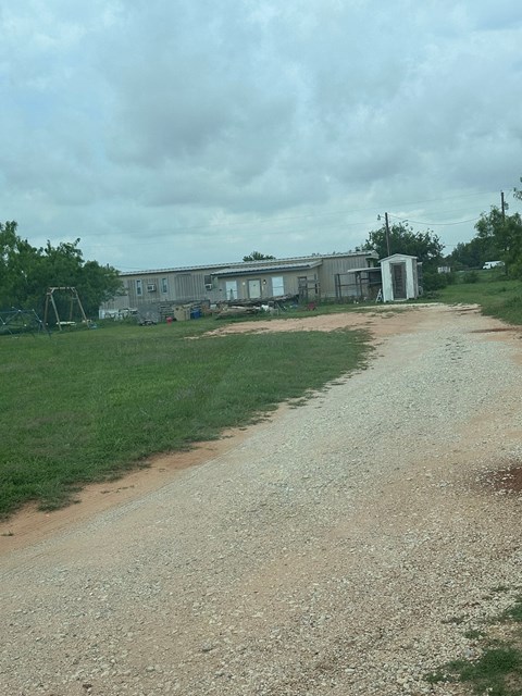 A gravel road leads to a house and a small shed.