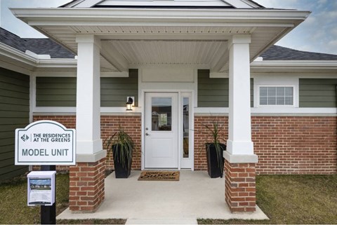 A house with a sign that says "The Residences at the Greens Model Unit".