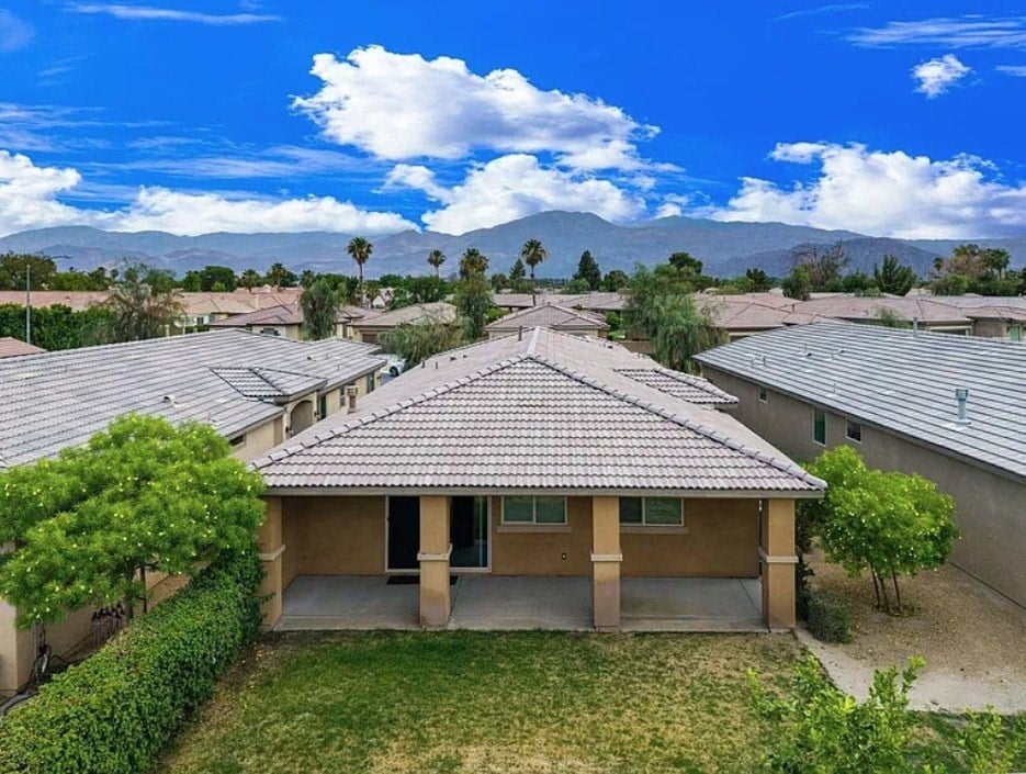 A house with a brown roof is surrounded by other houses and trees.
