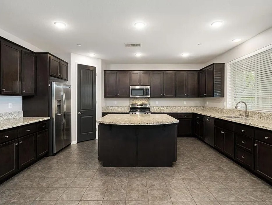 A kitchen with dark brown cabinets and a black island.