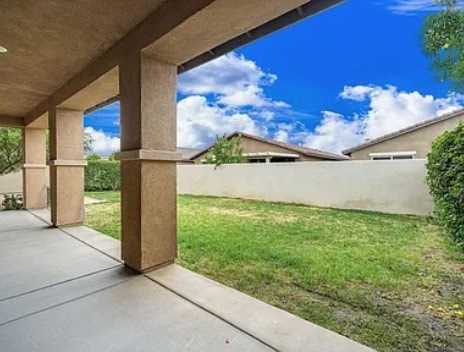 A concrete patio with a white wall and a blue sky with clouds in the background.