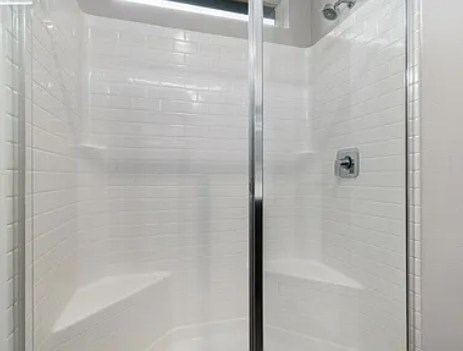 A white tiled shower stall with a glass door.