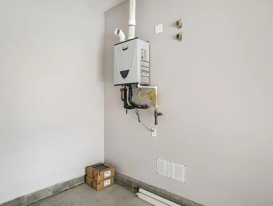 A wall-mounted heating system with pipes and a thermostat is installed in a room with a concrete floor and white walls.
