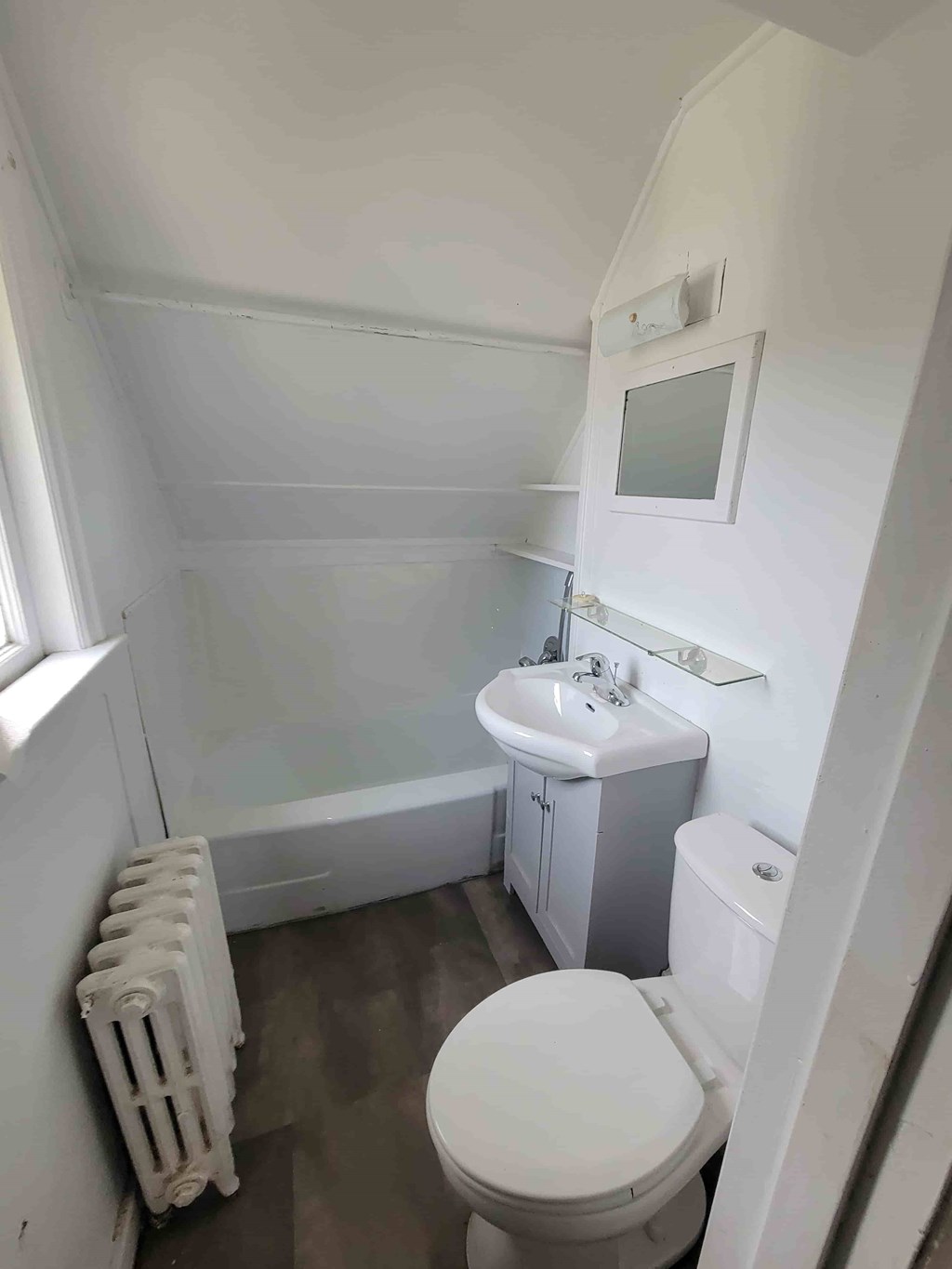 A white toilet sits in a small bathroom with a white sink and a white cabinet.