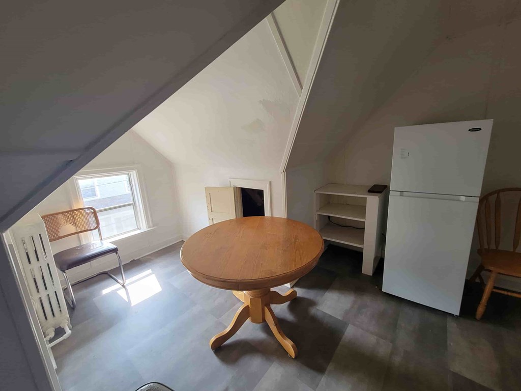A wooden table is in the middle of a room with a white refrigerator.