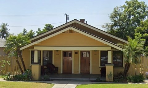 A yellow house with a brown door and a brown fence.