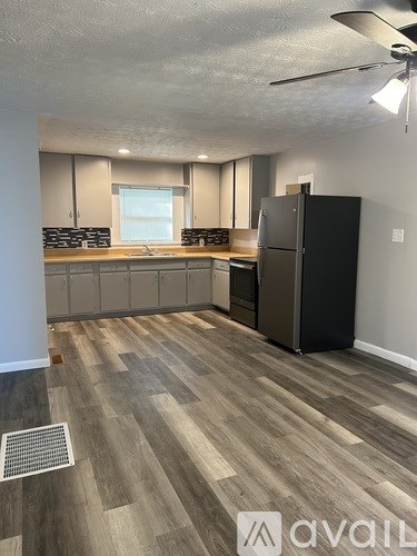 A kitchen with a black fridge and wooden flooring.