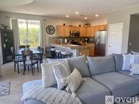 A living room with a grey couch and a kitchen in the background.