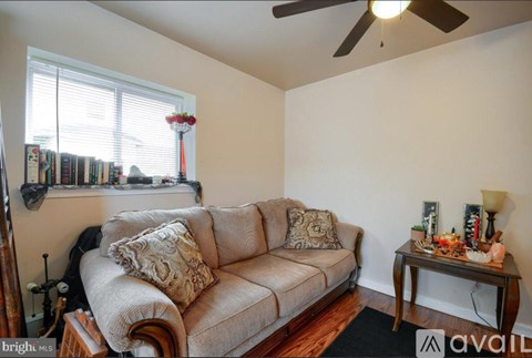 A living room with a couch, a table with a lamp and a vase on it, and a window with blinds.