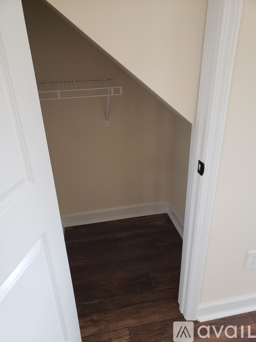 A white door is open to a room with a white wall and a wood floor.