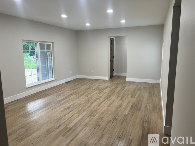 A room with wooden flooring and a window overlooking a green area.