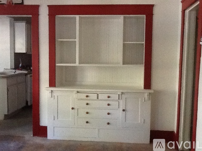 A white cabinet with drawers and a shelf is in a room with red trim.