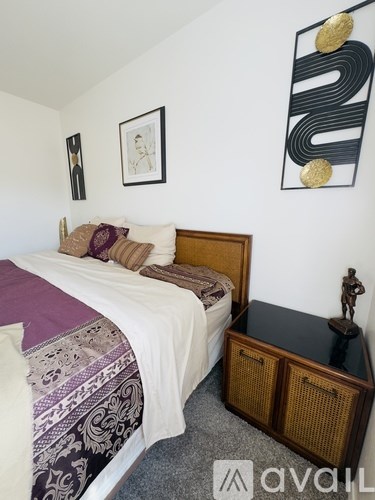 A bedroom with a bed, nightstand, and artwork on the wall.