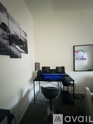 A black and white photo is hanging on the wall above a desk with a computer and a chair is in front of it.