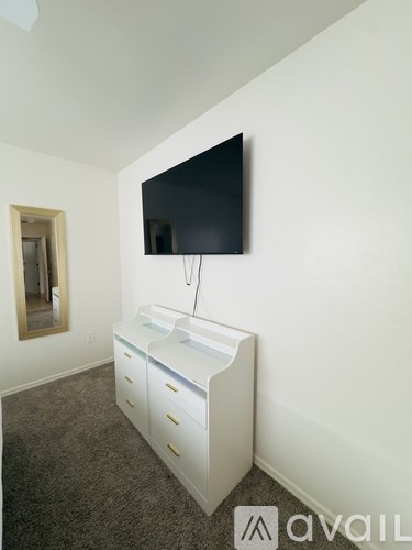 A white TV stand with a flat screen TV mounted on the wall above it.