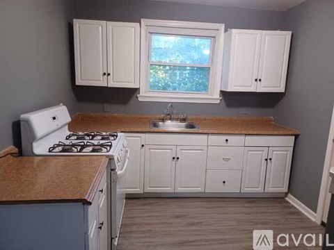 A kitchen with a white stove, sink, and cabinets.