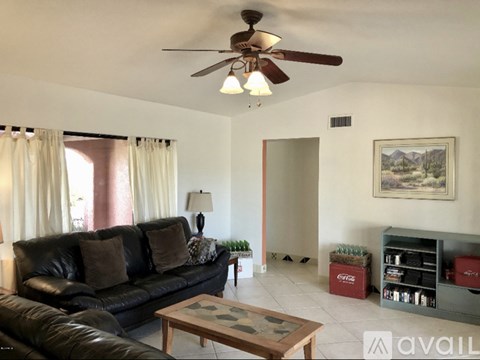 A living room with a black leather couch, a ceiling fan, and a painting on the wall.