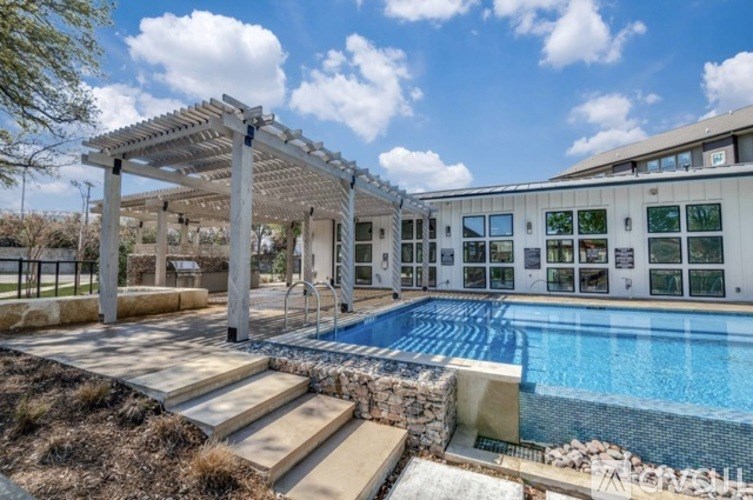 A pool area with a pergola and a building in the background.
