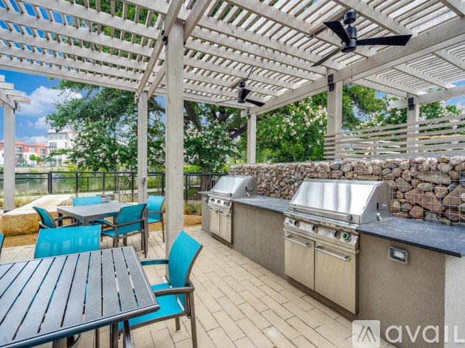 A patio with a table, chairs, and a grill under a pergola.