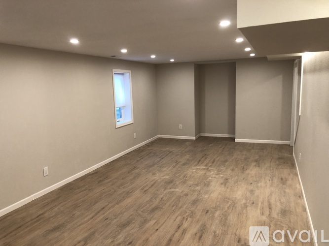 A spacious room with wooden flooring and a window on the left wall.