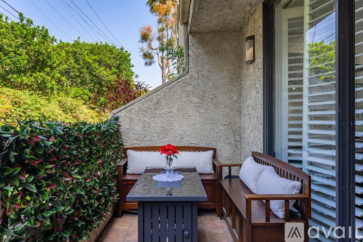 A patio with a bench, table, and a vase of flowers.
