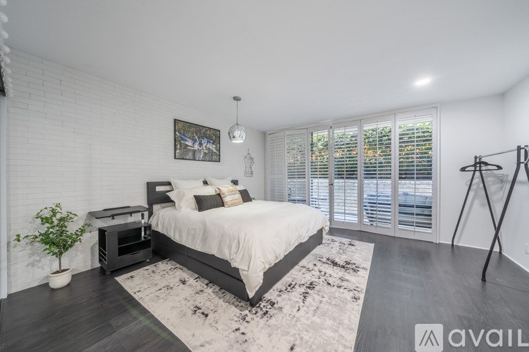 A bedroom with a large bed, a plant, and a painting on the wall.