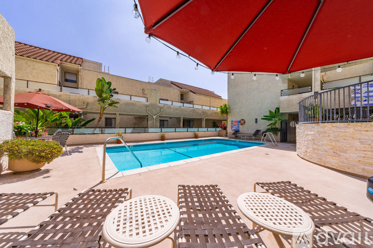 A pool area with sun loungers and a red umbrella.