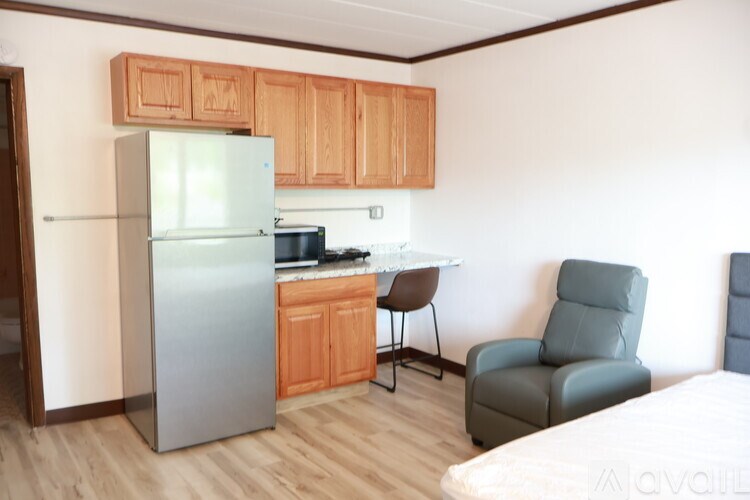 A kitchen with a refrigerator, a chair, and a bed.