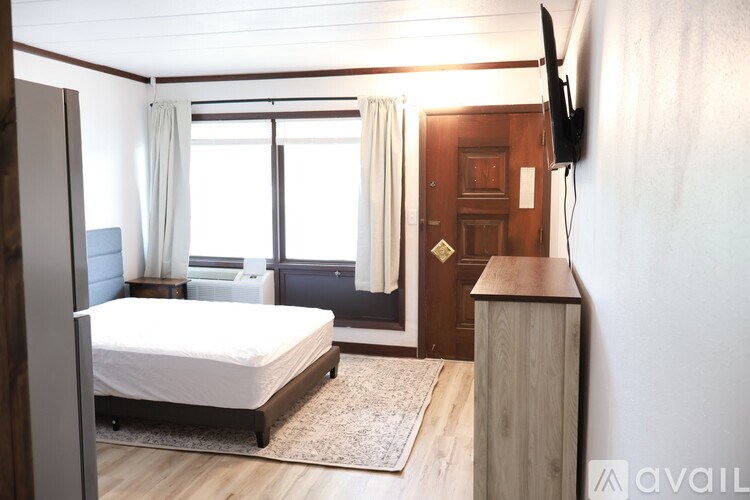 A bedroom with a bed, a TV, and a window with curtains.