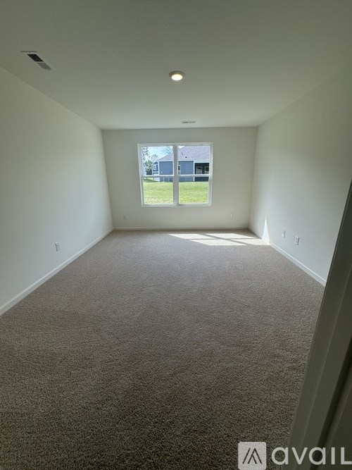 A carpeted room with a window overlooking a yard.